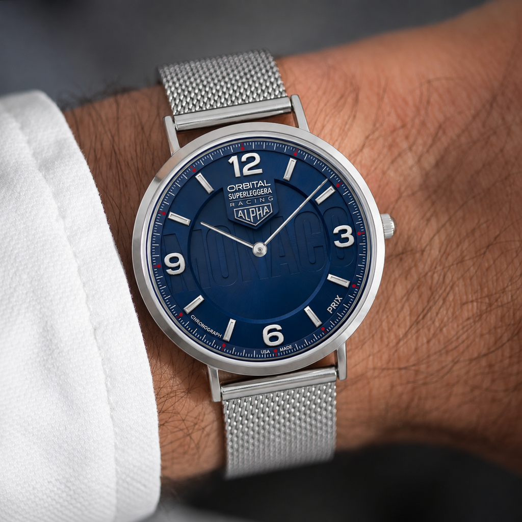 A close-up of a wrist wearing a Alpha Orbital Supermaestro watch with a deep blue dial and a silver stainless steel mesh bracelet.
