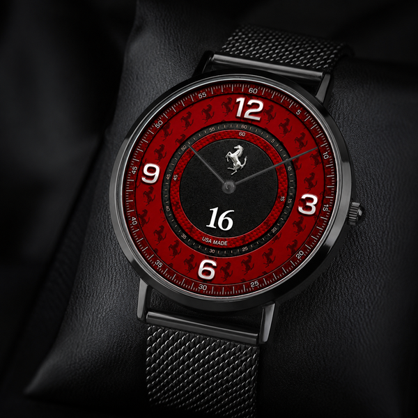 A luxury-style wristwatch with a black mesh strap and a red dial featuring a racing emblem and '16' at the center, resting on a black leather surface.