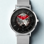 A silver stainless steel mesh-strand watch with a round silver case and a black dial featuring a red bat symbol over a dark, moody Batman-themed illustration.