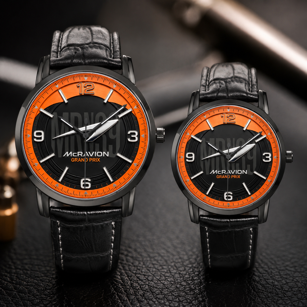 Two matching wristwatches with black leather straps and black dials featuring bright orange bezels and white numerals. The larger watch is in front of the smaller one, both branded MCRAVION GRAND PRIX, set against a dark textured surface.