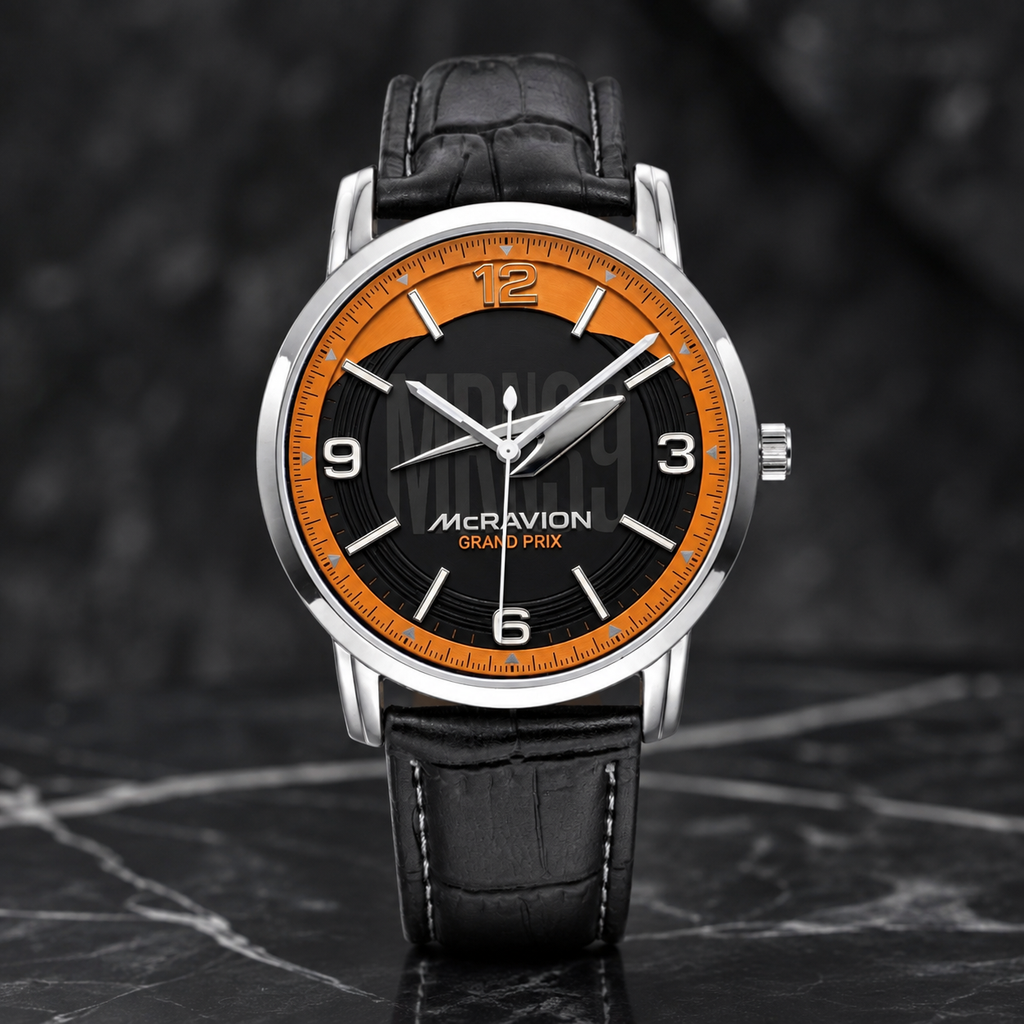 A wristwatch with a silver-tone case, black dial, bright orange ring around the dial, and a black leather strap, photographed on a dark marble-like surface.