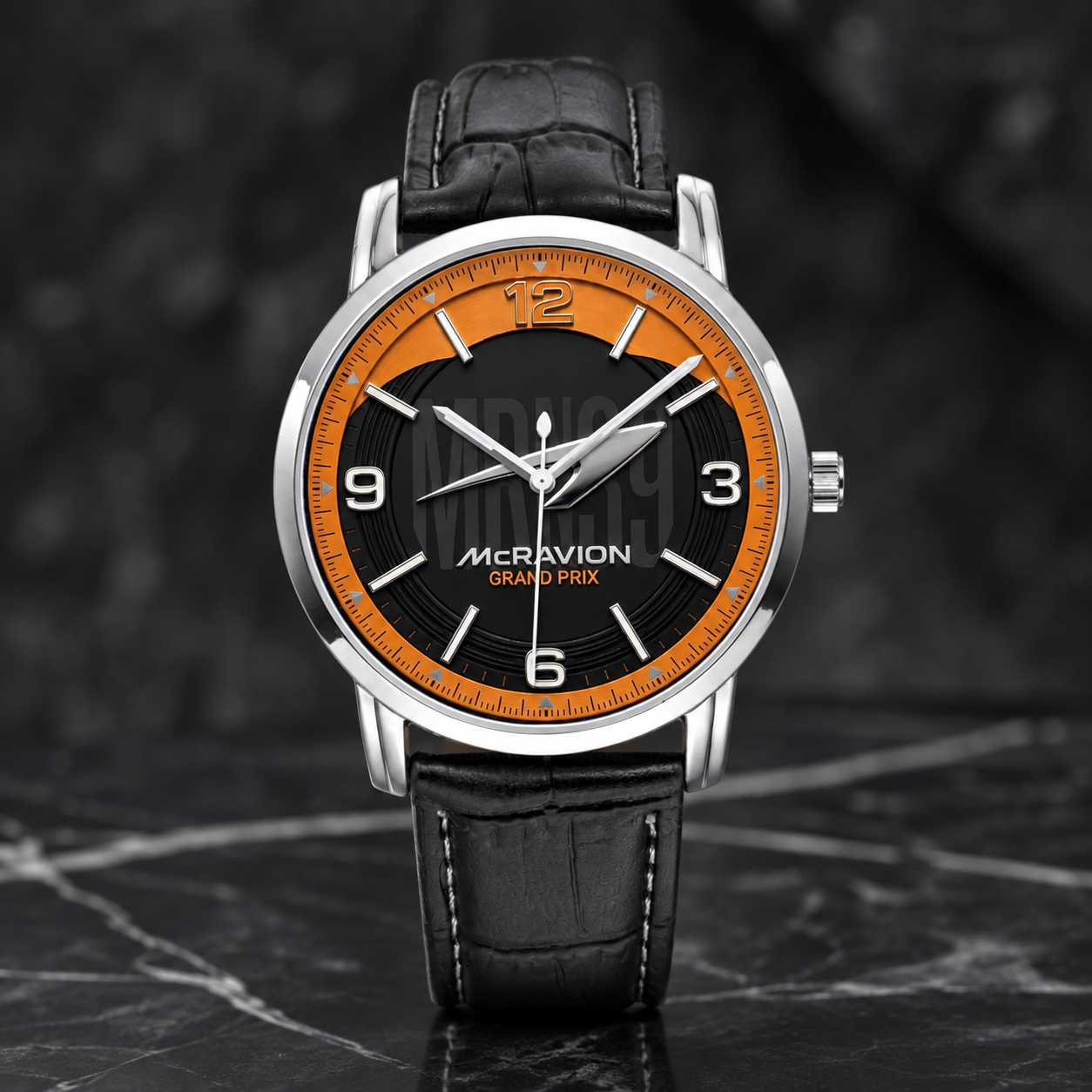 A wristwatch with a silver-tone case, black dial, bright orange ring around the dial, and a black leather strap, photographed on a dark marble-like surface.