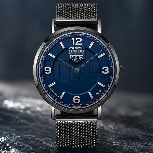 A close-up studio shot of a Joventra Monaco Orbital watch with a dark blue dial, silver-toned case, and dark gray mesh strap, set against a dark textured background. The dial features the Orbital Superleggera branding.