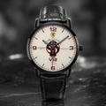 A Joventra Rosso Corsa V12 watch with a black leather strap, black case, and a cream-colored dial featuring red numerals, a racing emblem, and a central red and black graphic.