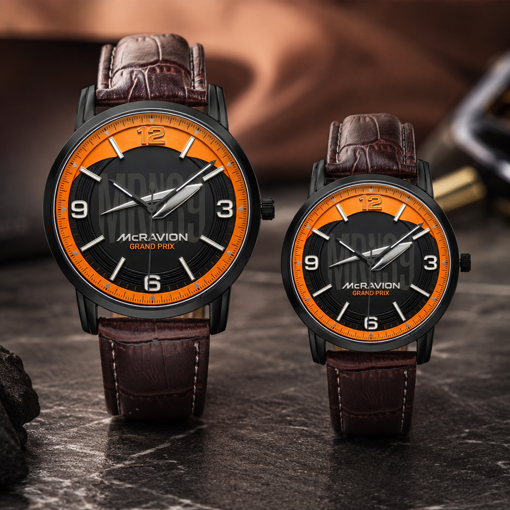 Two matching wristwatches displayed side by side on a dark stone surface. Each watch has a black case, a black dial with a bright orange ring around the bezel, silver-tone hands and markers, and a dark brown leather strap.