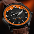 A close-up of a Mcravion Grand Prix wristwatch featuring a black and vibrant orange dial with silver-tone hands and markers, paired with a brown leather strap.
