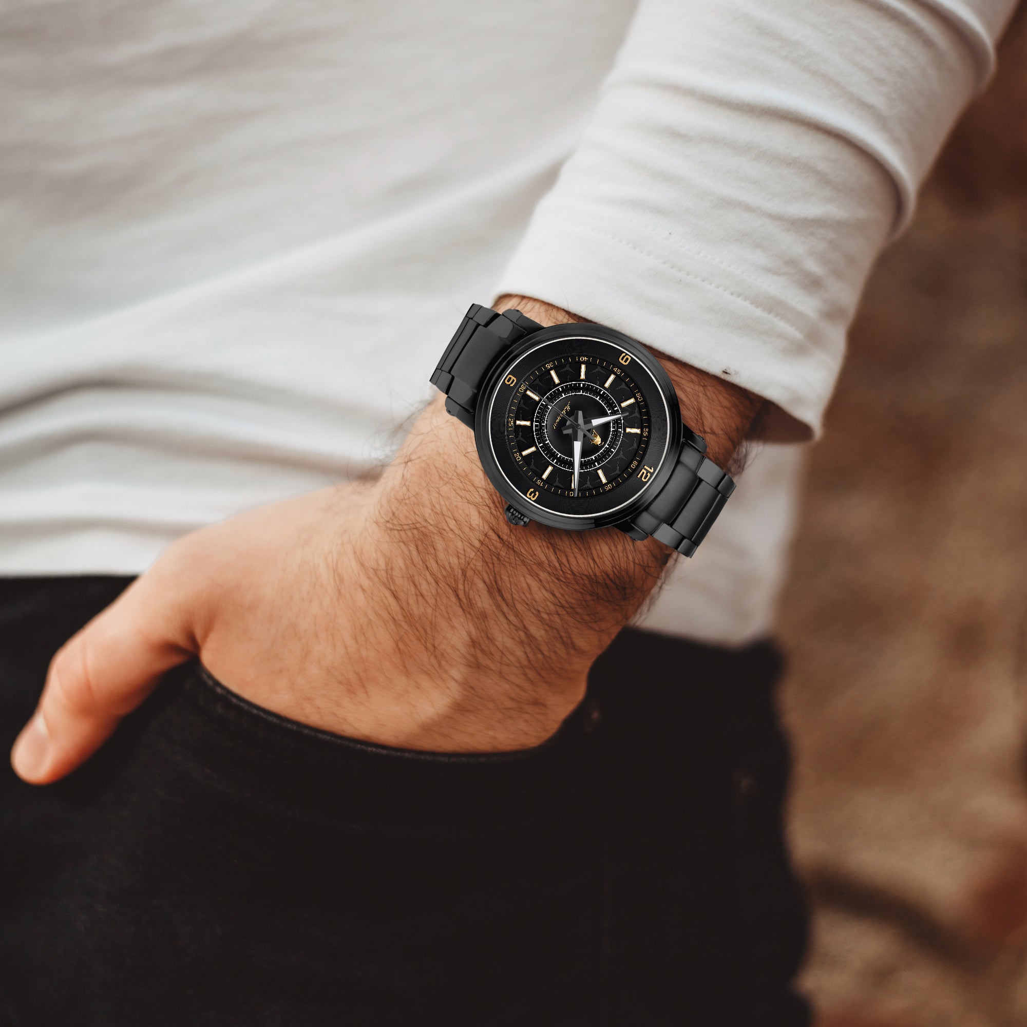A close-up of a person's wrist wearing a black smartwatch with a black strap and gold-tone details, paired with a white long-sleeve shirt and black pants.