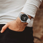 Silver watch with black face on a wrist, blurred background