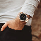 A close-up of a man's wrist wearing a modern analog watch with a black dial and rose gold-toned metal case and bracelet.