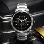 A silver stainless steel wristwatch with a black dial, gold-tone numerals and hands, and a matching metal link bracelet, displayed on a dark marble surface with a blurred car interior in the background.