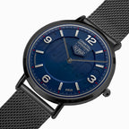 Analog wristwatch with a textured dark blue dial, black case, and a black mesh strap, shown on a clean white background.