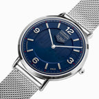 A close-up studio shot of a ALPHA Orbital PRIX stainless steel watch with a textured blue dial and a silver mesh strap on a white background.