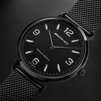 A close-up studio shot of a black Mercedes-AMG wristwatch with a black mesh metal band, featuring silver-tone numerals and hands with subtle orange accents on the dial.