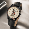 A wristwatch with a black leather strap, black case, and a cream-colored dial featuring a cartoon panda character. The watch is photographed on a reflective metallic surface.