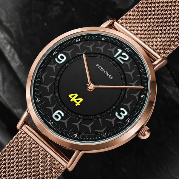 A close-up of a Petronas wristwatch with a rose gold mesh strap, a black dial with white Arabic numerals, and a yellow '44' display on a dark textured background.