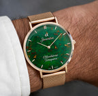 A close-up of a wrist wearing a gold-tone mesh Joventra Bloodstone Timepiece watch with a green dial featuring gold flecks.