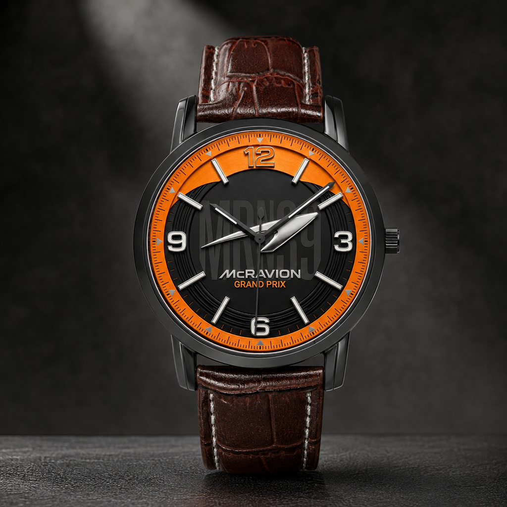 A luxury wristwatch by McRavion Grand Prix, featuring a dark gray case, a black dial with a vibrant orange inner ring and white numerals, and a brown crocodile-embossed leather strap.