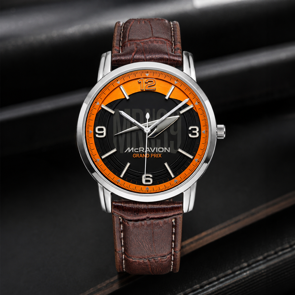 A wristwatch with a brown leather strap, a silver-toned case, and a black dial featuring a bright orange inner ring and orange numerals. The brand name 'MCRAVION' is printed on the dial.