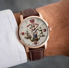 A close-up of a wrist wearing a Popeye the Sailor themed watch with a rose gold case, brown leather strap, and a detailed nautical dial featuring Popeye and a lighthouse.
