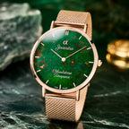 A Joventra Bloodstone Timepiece watch with a rose gold mesh strap and a green dial featuring natural bloodstone inclusions, displayed on a dark green marble surface.