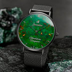 A Joventra Bloodstone Timepiece watch with a green malachite-patterned dial and a dark gray mesh strap, displayed on a dark textured surface with mineral rocks in the background.