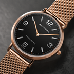 A close-up of a Mercedes-Benz AMG wristwatch featuring a black dial, rose gold case, and matching rose gold mesh strap, set against a dark textured background.