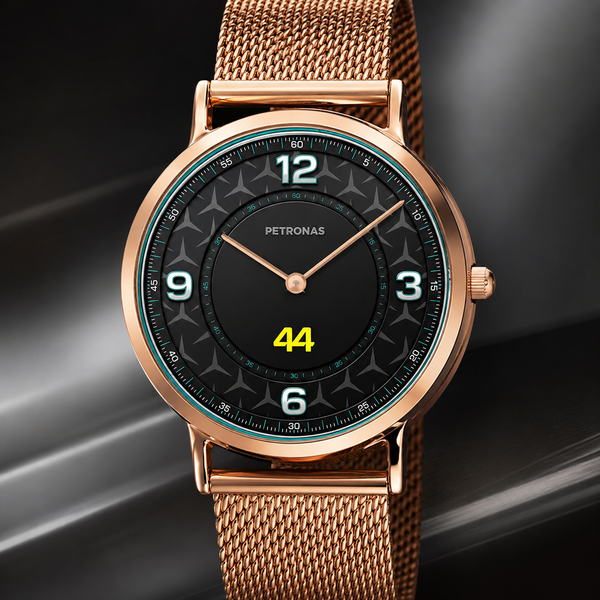 A Petronas wristwatch with a rose gold mesh strap, a round rose gold case, and a black dial featuring white Arabic numerals and a yellow '44' indicator, set against a dark gray background with light streaks.